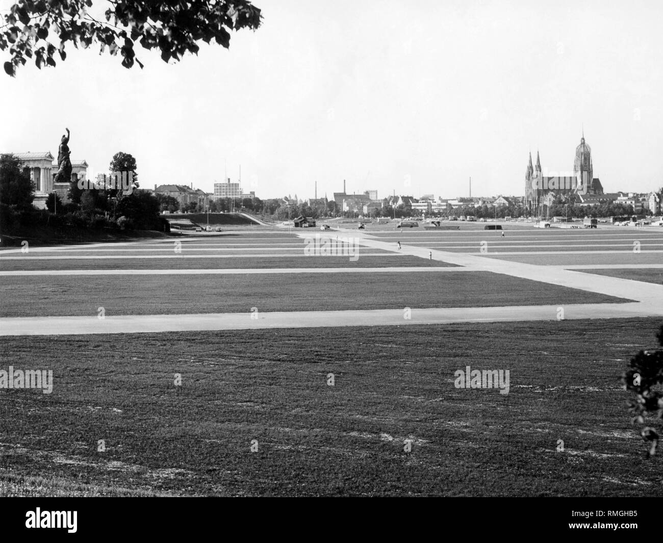 Auf der Theresienwiese in München mit grünem Rasen und Wege. Auf der linken Seite, die Statue von Bayern, rechts im Hintergrund die Katholische Pfarrkirche St. Paul. Stockfoto