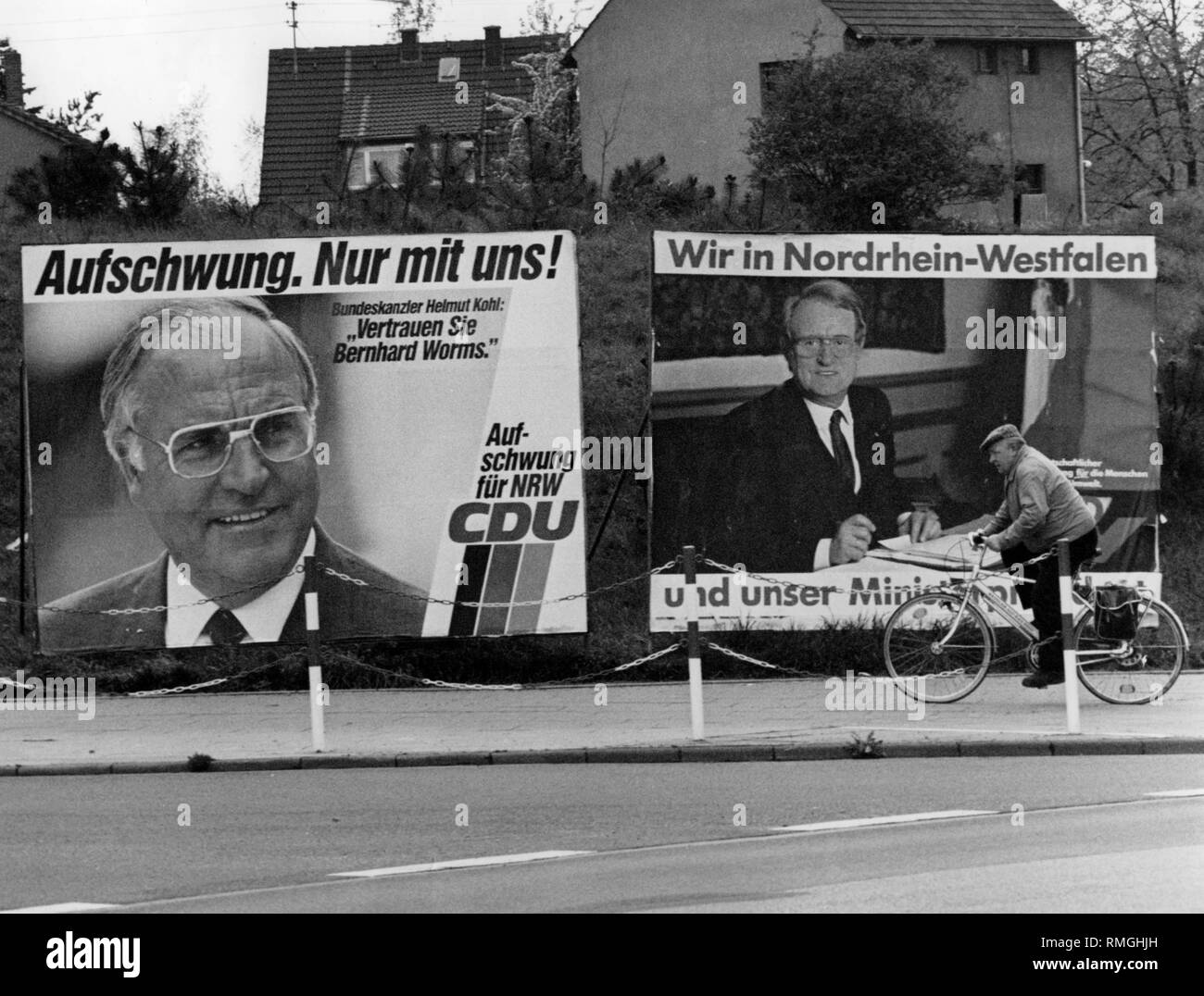 Zwei wahl Plakate für die Landtagswahl in Nordrhein-Westfalen am 12.5.1985 auf einer Straße. Auf der linken Seite ist ein Plakat der CDU mit der Inschrift: "die wirtschaftliche Erholung. Nur mit uns! Revival für die NRW-CDU". Neben einem Portrait von Helmut Kohl mit einem Zitat: "Vertrauen Bernhard Worms.". Direkt daneben ein Plakat der SPD. Es lautet: "Wir in Nordrhein-Westfalen und unser Minister Präsidenten'. Zusätzlich ein Bild von Johannes Raus. Ein Teil der Inschrift der Poster ist verdeckt von einem vorbeifahrenden Radfahrer. Stockfoto