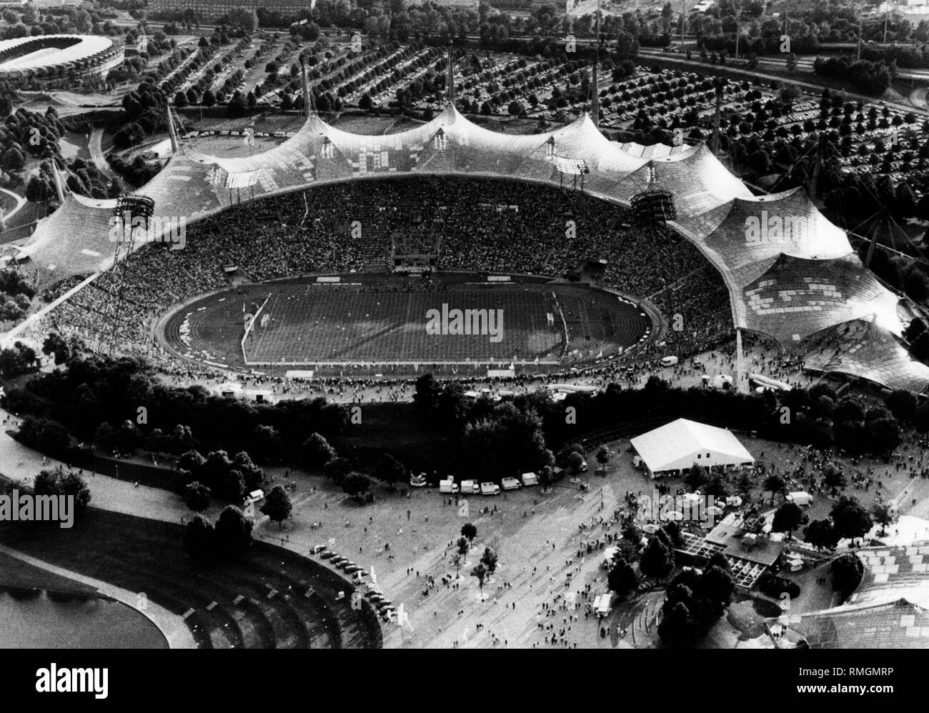 Blick auf das Münchner Olympiastadion während der Vorrunde der Fußball-Europameisterschaft 1988 in Deutschland zwischen der Bundesrepublik Deutschland und Spanien. Endergebnis: 2:0. Im Vordergrund von links: olympiasee See, Coubertinplatz, Olympiahalle und Biergarten. Im Hintergrund der Olympischen Radstadion (links) und die Tiefgarage. Stockfoto
