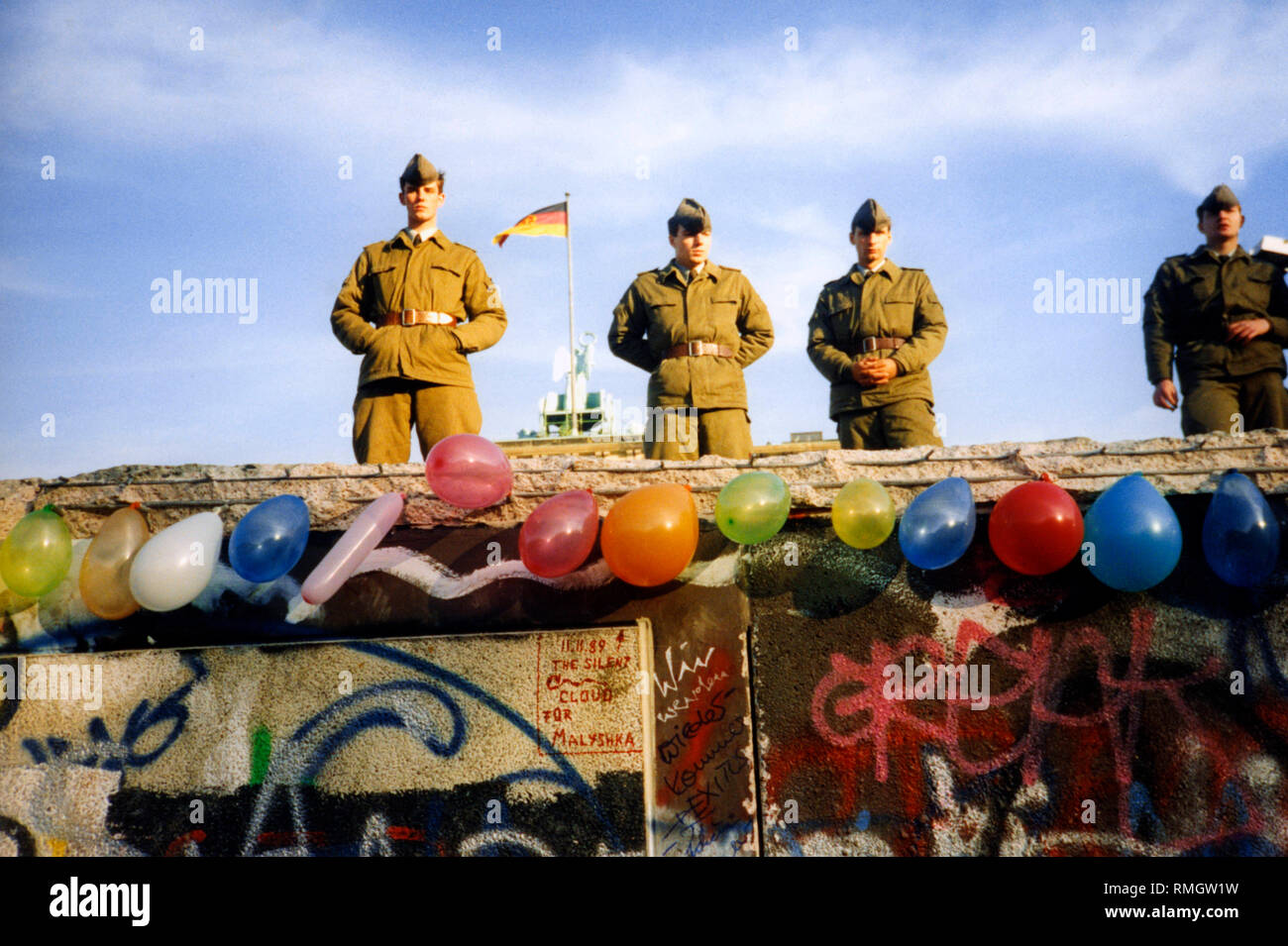 Vier grenzsoldaten an der Berliner Mauer. Hinter ihnen, das Brandenburger Tor mit der Deutschland Fahne. Ballone sind an der Wand befestigt. Stockfoto