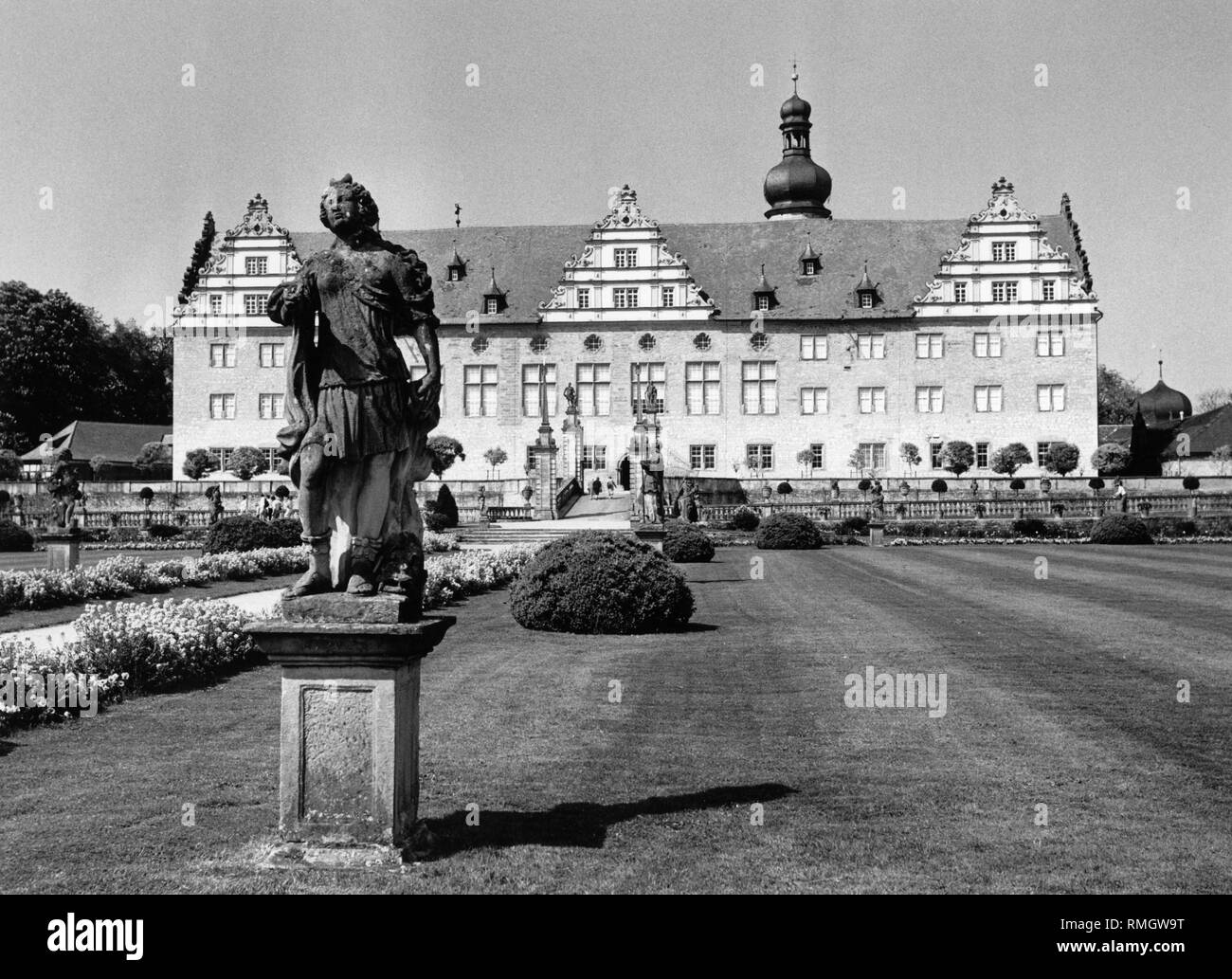 Blick durch den Garten auf der Vorderseite des Renaissance Schloss Weikersheim. Im Vordergrund steht eine steinerne Statue. Stockfoto