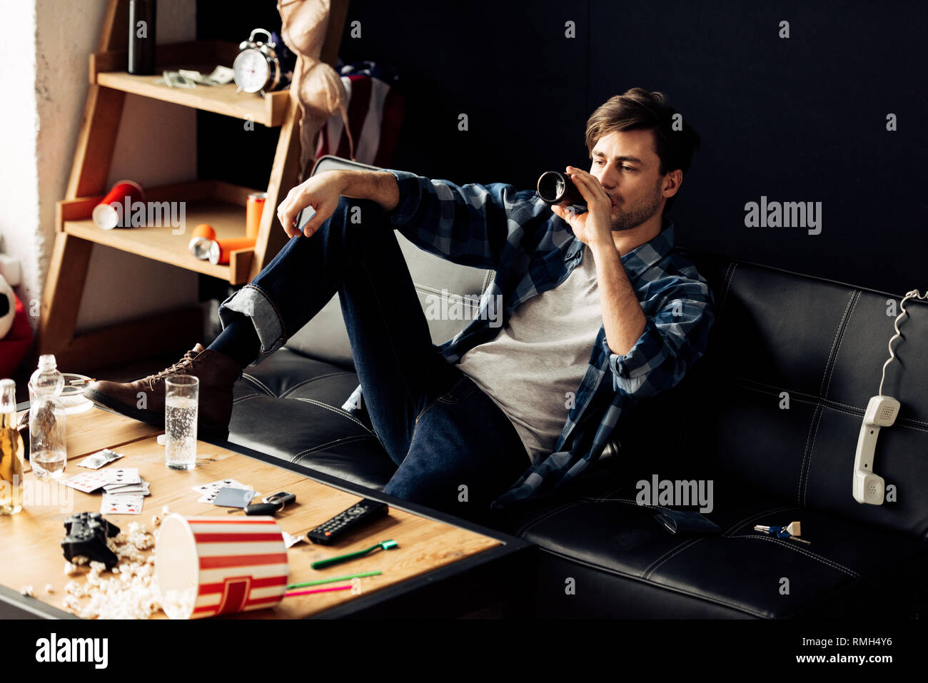 Betrunkener Mann sitzt auf dem Sofa und trinken Bier an unordentliche Wohnung Stockfoto
