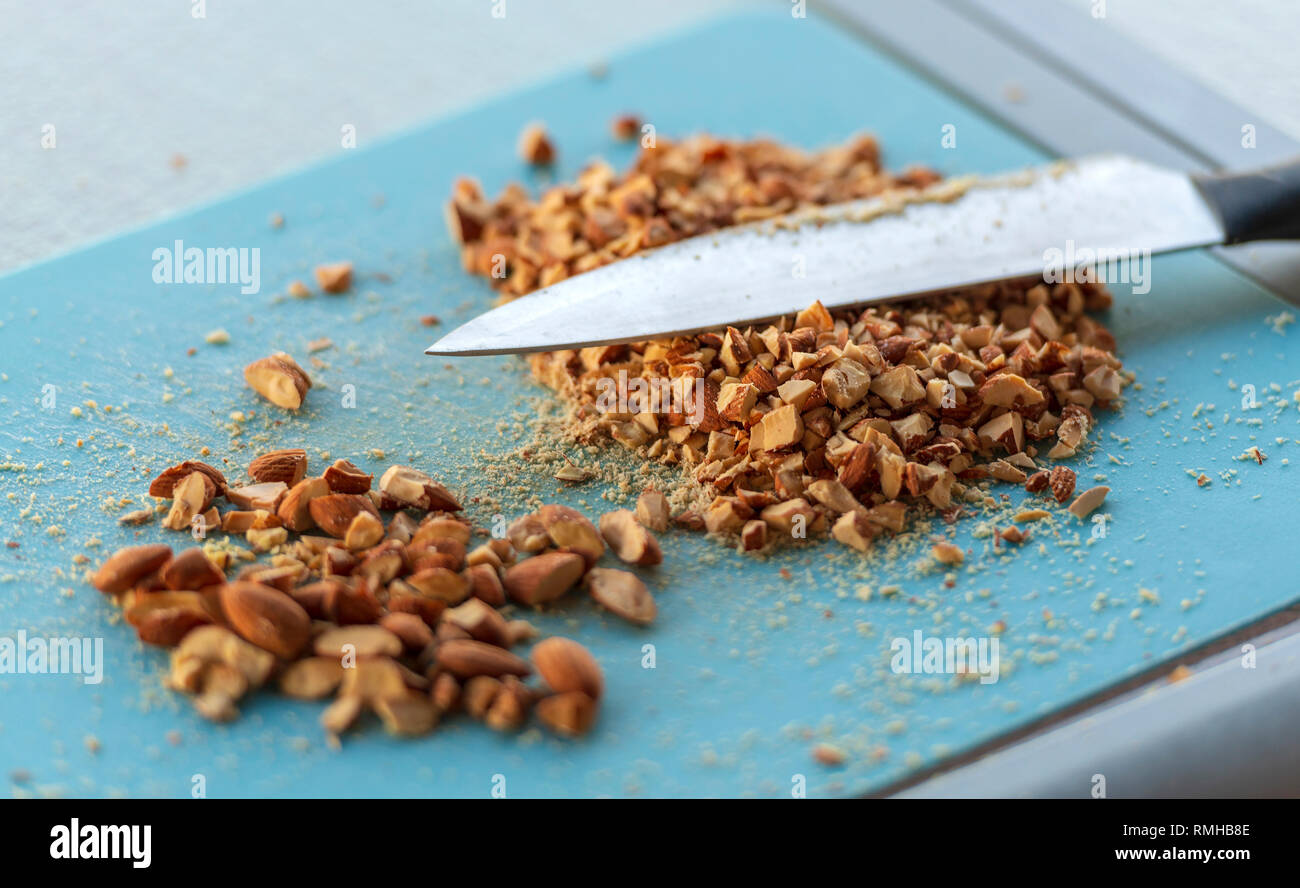 Gebrannte Mandeln gehackt und auf einem blauen Schneidebrett in flachen Fokus zerquetscht Stockfoto