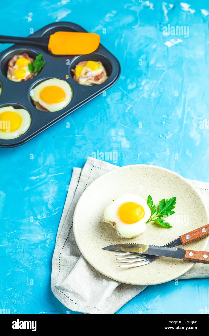 Gebackene Eier in der Licht- und Backformen. Portioniert Auflauf von Speck und Eier im italienischen Stil. Blauer Beton Tischfläche Hintergrund. Stockfoto