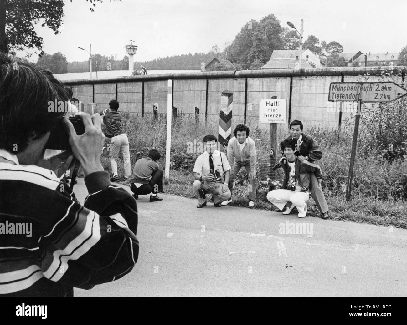 Eine Gruppe japanischer Touristen nehmen Fotos an der DDR-Grenze in Bayern. Neben einem Warnzeichen der Bundesgrenzschutz ein Wegweiser zu Muenchenreuth und Tiefendorf in Hof. Im Hintergrund, ein Wachturm. Stockfoto