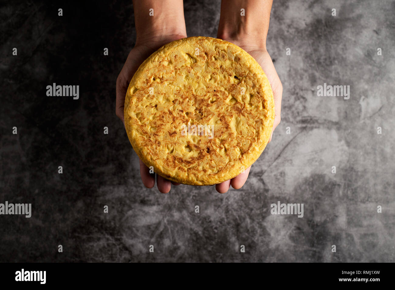 Hohe Betrachtungswinkel von einem kaukasischen Mann mit einer typischen Tortilla de patatas, spanisches Omelette, auf seinen Händen, auf einer grauen Stein Oberfläche Stockfoto