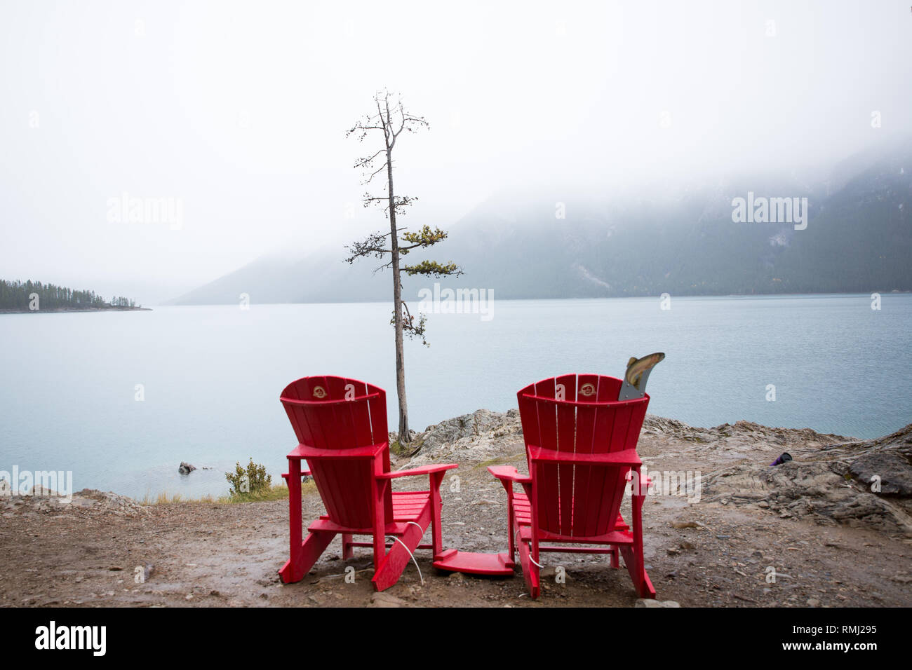 Zwei roten Stühlen mit Blick auf Lake Minnewanka an einem nebligen Tag in Banff National Park, Kanada Stockfoto