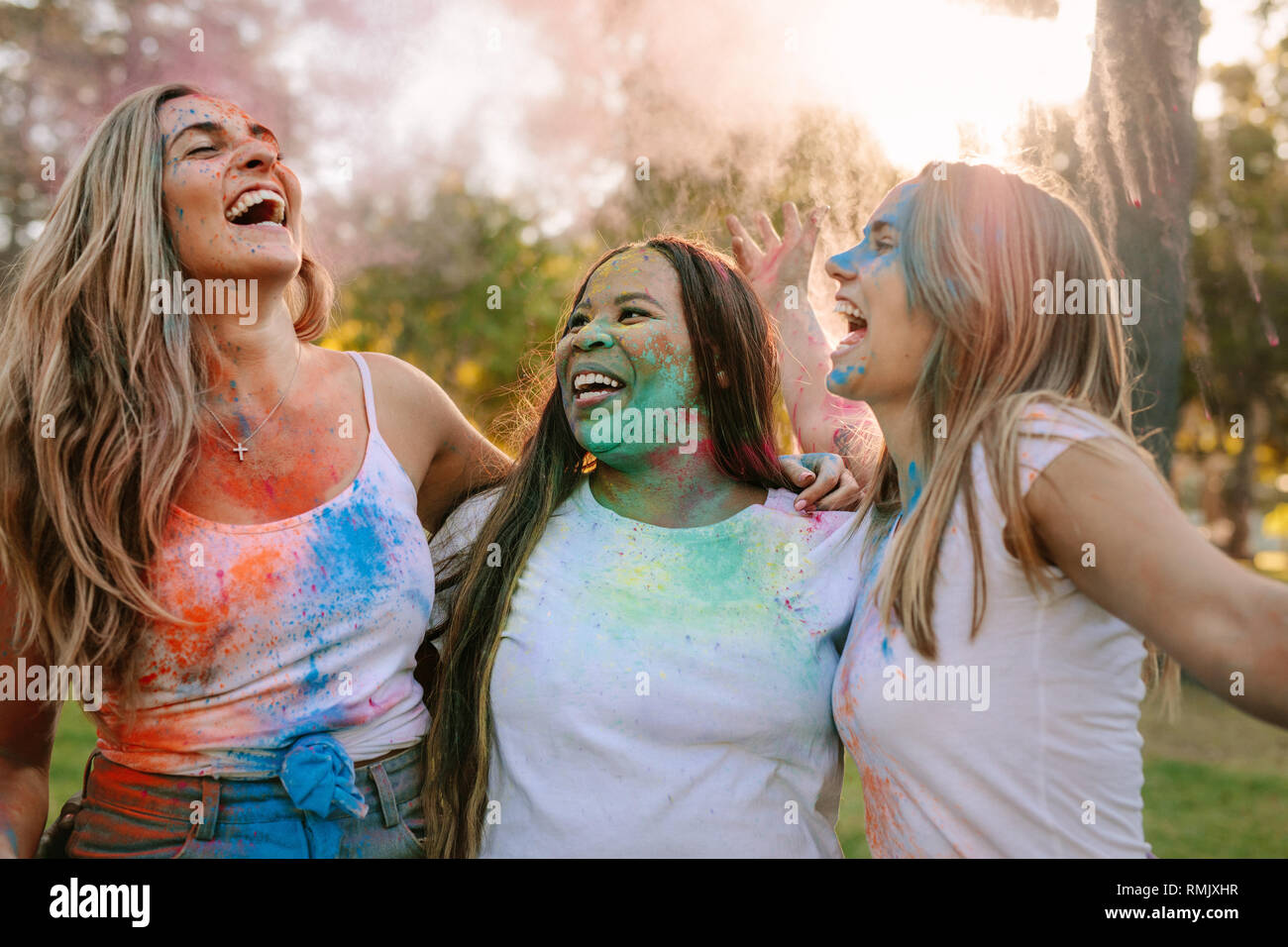 Drei Frauen Spaß Holi spielen mit Farben auf ihrem Gesicht spritzte. Freunde genießen Holi in einem Park und Lachen in der Freude. Stockfoto