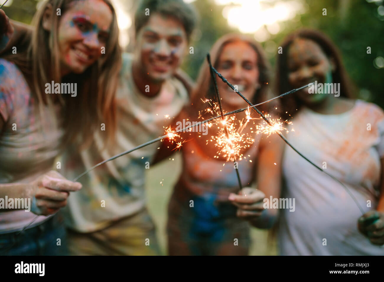 Mann mit Frauen, die Freunde in einem Park stehen und brennenden Feuer funkelt. Gruppe von Freunden genießen Feuerwerk zusammen mit Spielen von Holi. Stockfoto