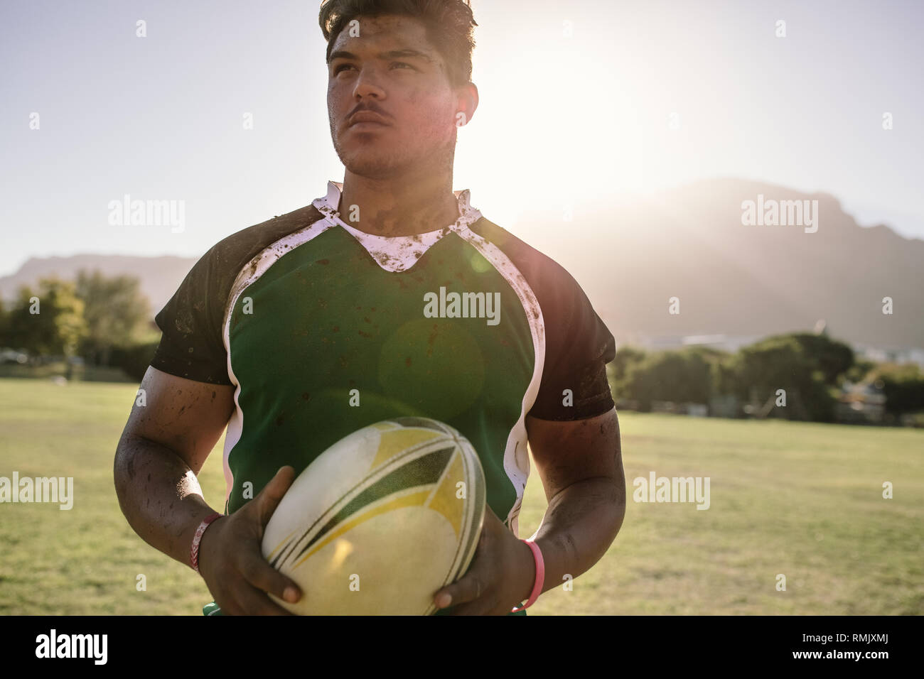 rugbyspieler, der einen Rugbyball auf dem Sportplatz hält. Junger Sportler, der einen Rugbyball mit schmutziger Uniform hält. Stockfoto