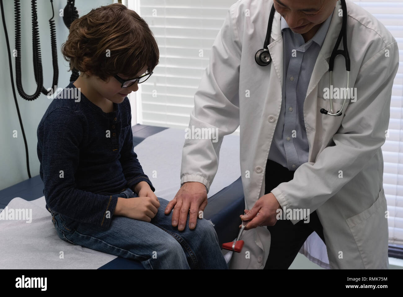 Jungen asiatischen männlicher Arzt Prüfung der kaukasischen jungen Patienten Knie in einer Klinik Stockfoto