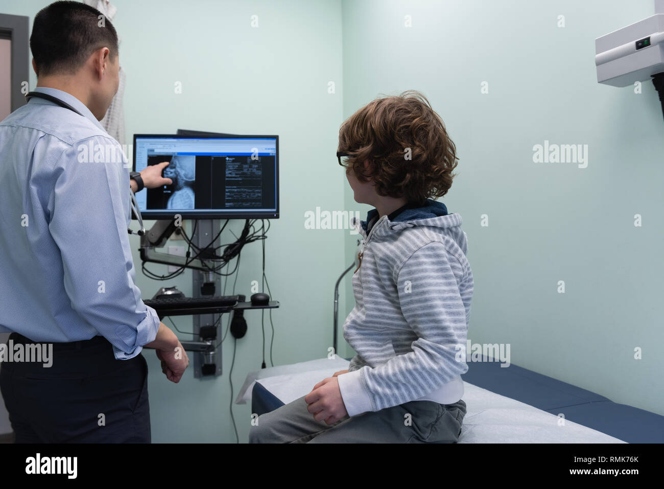 Jungen asiatischen männlicher Arzt angezeigt mit kaukasischen jungen Patient x-ray auf Bildschirm Stockfoto