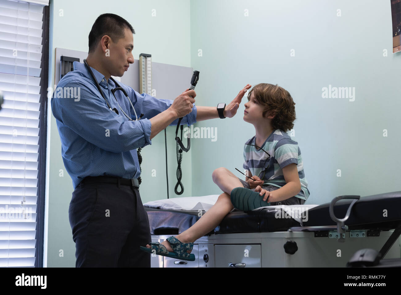 Jungen asiatischen männlicher Arzt Untersuchung einer kaukasischen jungen Patienten Auge mit Werkzeug in einer Klinik Stockfoto