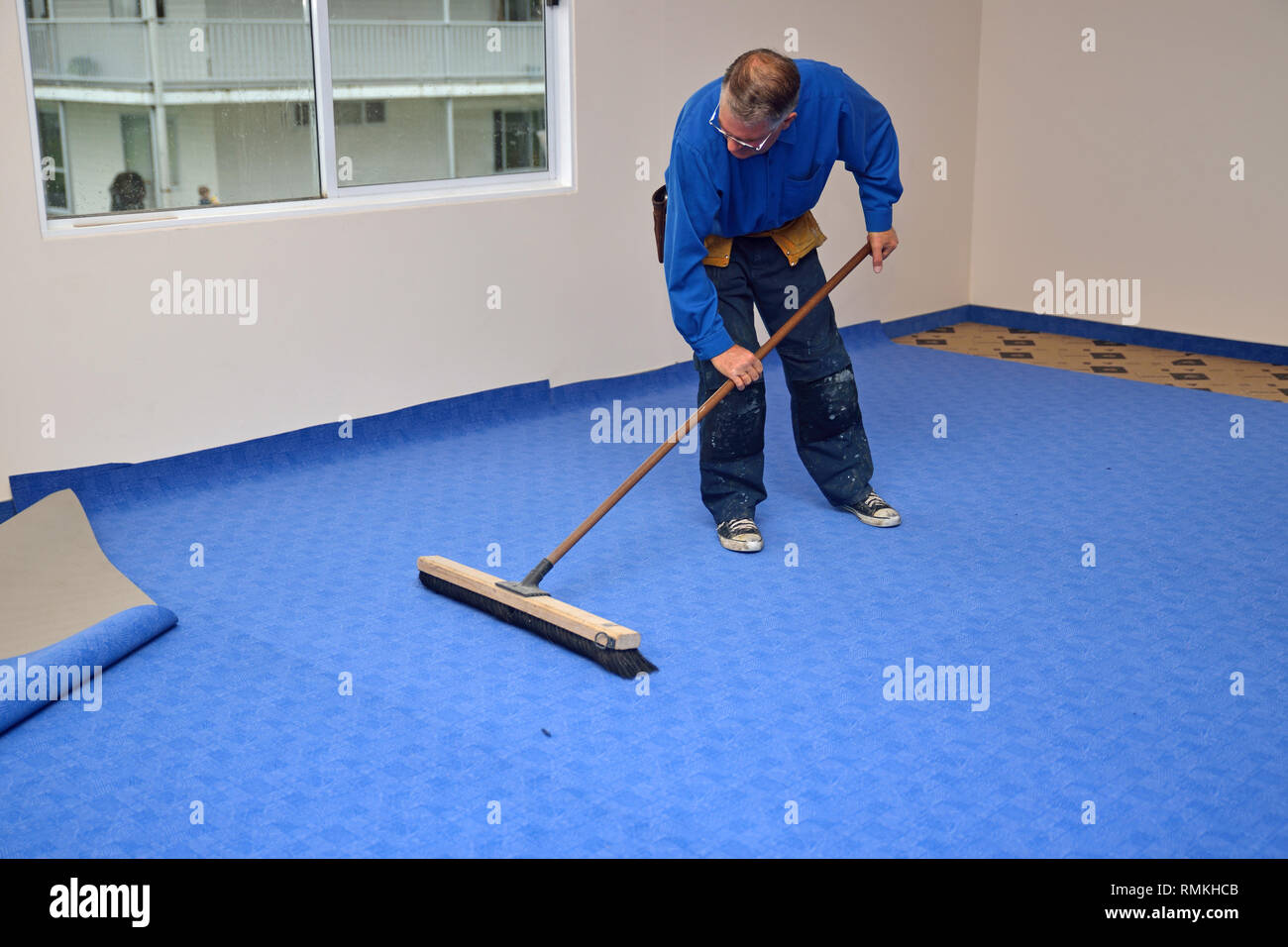 Eine Floorlayer verwendet sorgfältig einen breiten Besen um zu glätten die Falten in seinem neu verlegten Teppich Stockfoto