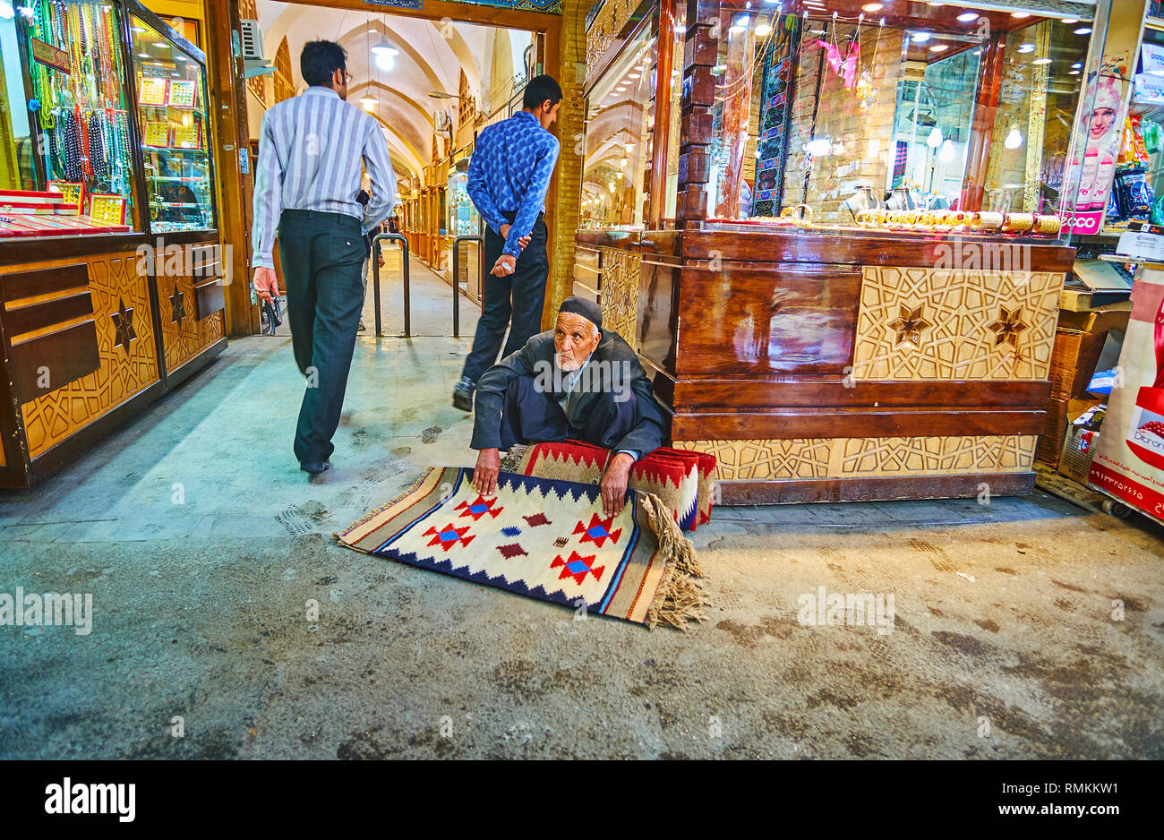 ISFAHAN, IRAN - 21. Oktober 2017: Die älteren Kaufmann bietet kleinen Wollteppichen, sitzend auf dem Boden neben Juweliergeschäfte von Grand (Soltani, Qey Stockfoto