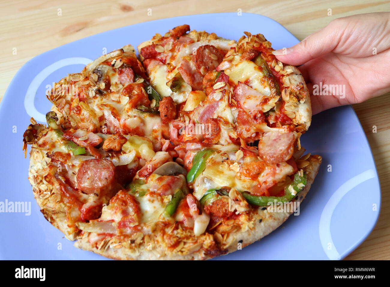 Woman's Hand Kommissionierung ein Stück italienische Wurst mit Paprika Pizza auf blauem Teller serviert Stockfoto