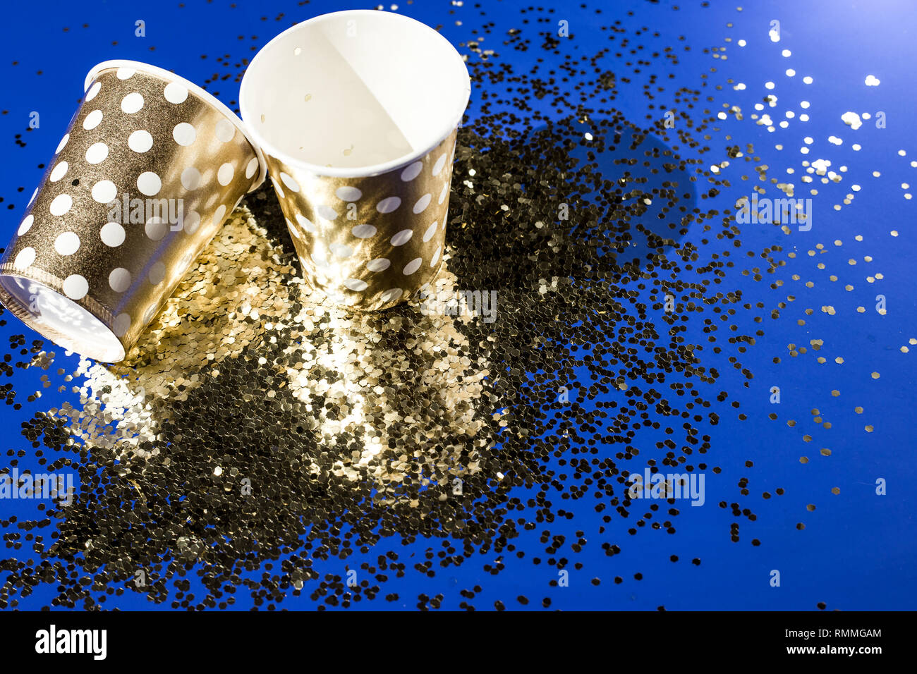 Golden Pappbecher für Geburtstagsfeier mit goldenen Konfetti auf blauem Hintergrund. Stockfoto