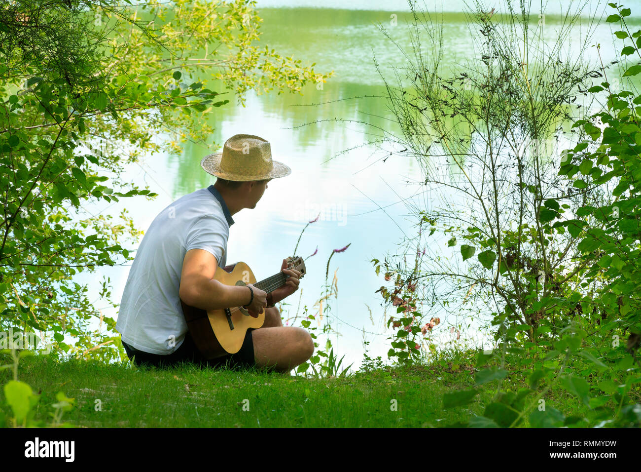 Junger Mann an der Gitarre von einem Teich im Sommer Stockfoto