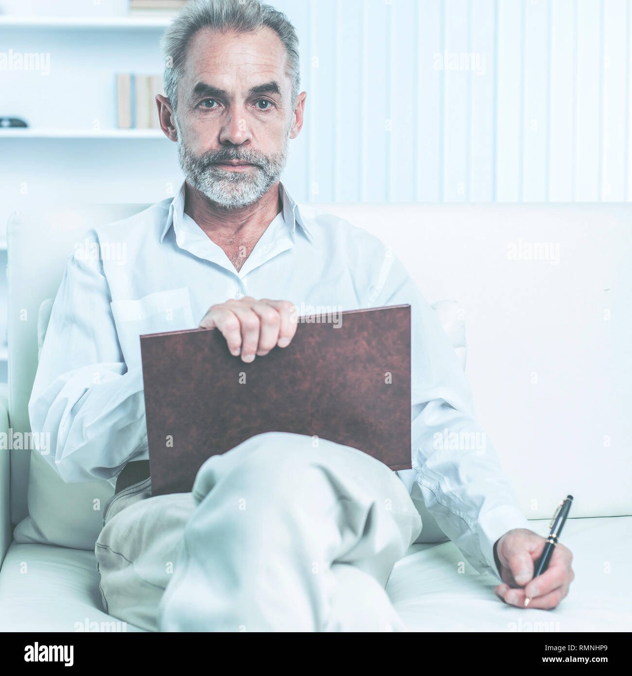 Erfolgreicher Geschäftsmann mit Stift und Business Magazine, auf einem Stuhl sitzend das moderne Büro Stockfoto