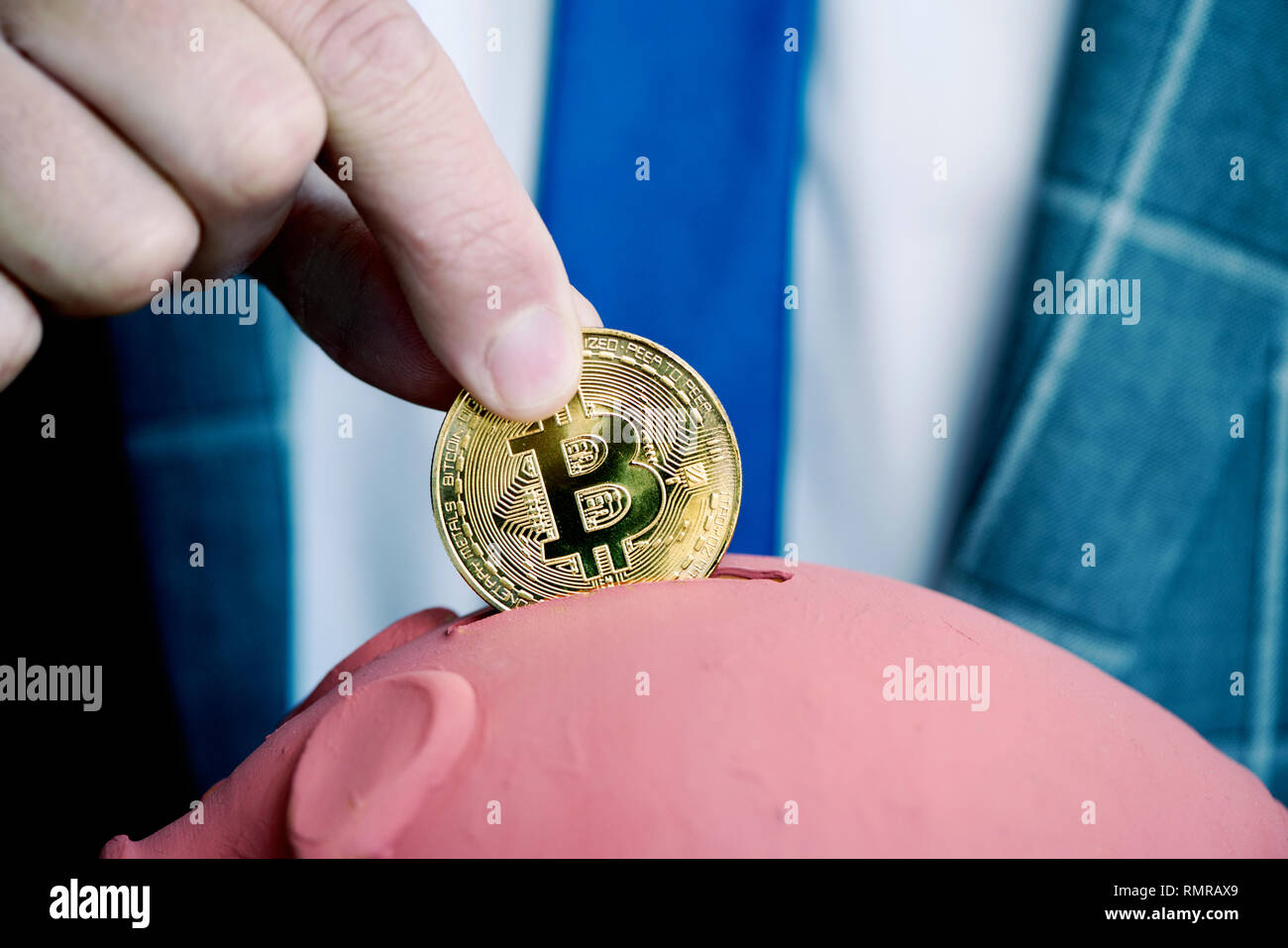 Nahaufnahme eines jungen kaukasischen Geschäftsmann, in einem eleganten grauen Anzug, Einfügen eines Bitcoin in ein Schwein-förmige piggy Bank Stockfoto