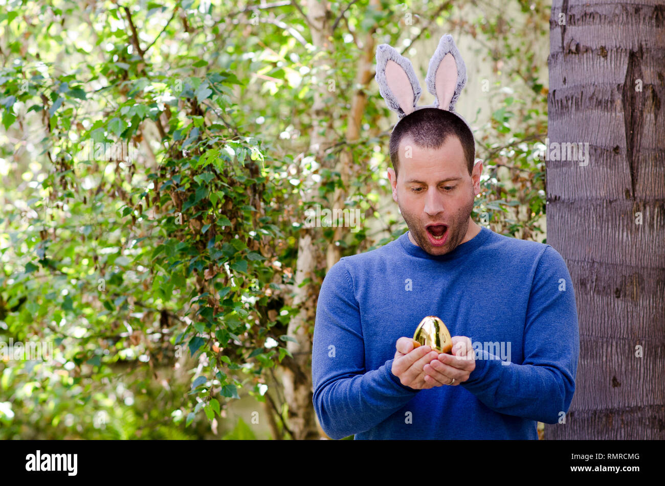 Eine Osterüberraschung! Mann hält eine goldene Osterei mit Hasenohren auf seinem Kopf. Stockfoto