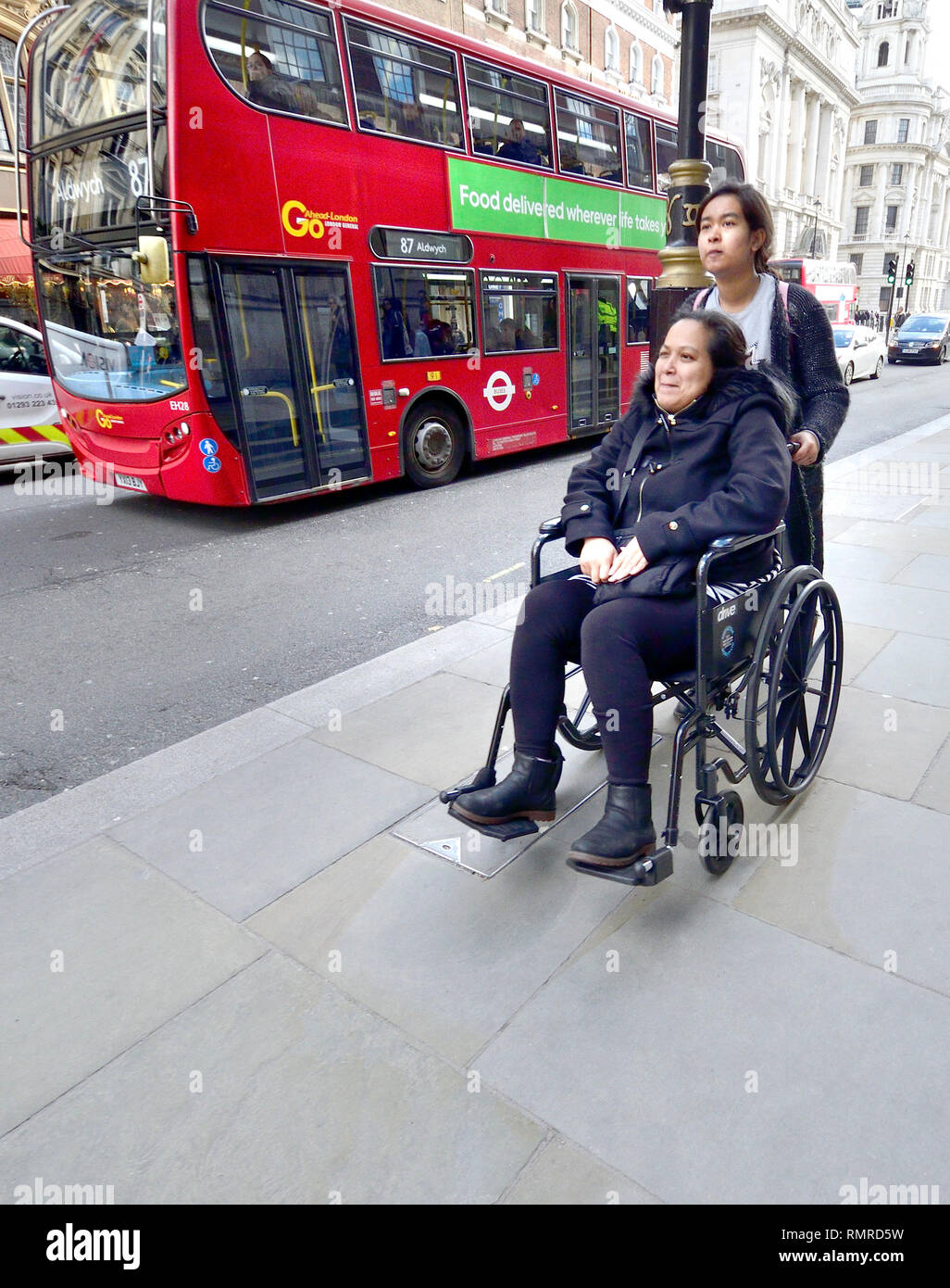 London, England, UK. Frau, die in einem Rollstuhl in Whitehall geschoben, wie ein Bus fährt Stockfoto