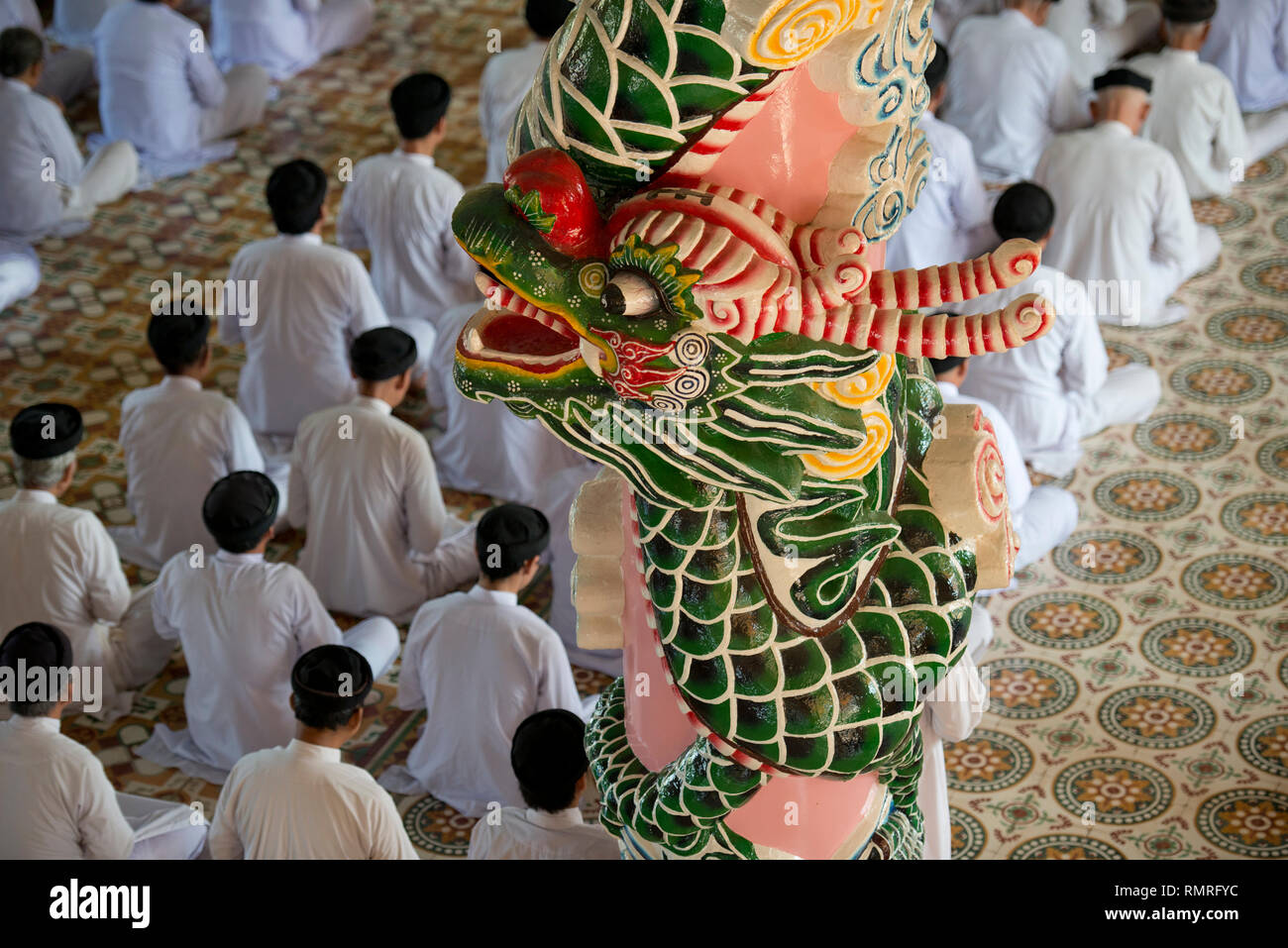 Caodaist jünger, während der Zeremonie sitzend durch bunte Säulen mit Drachen, Cao Dai Tempel, Tay Ninh (100 km NW von HCMC), Vietnam Stockfoto