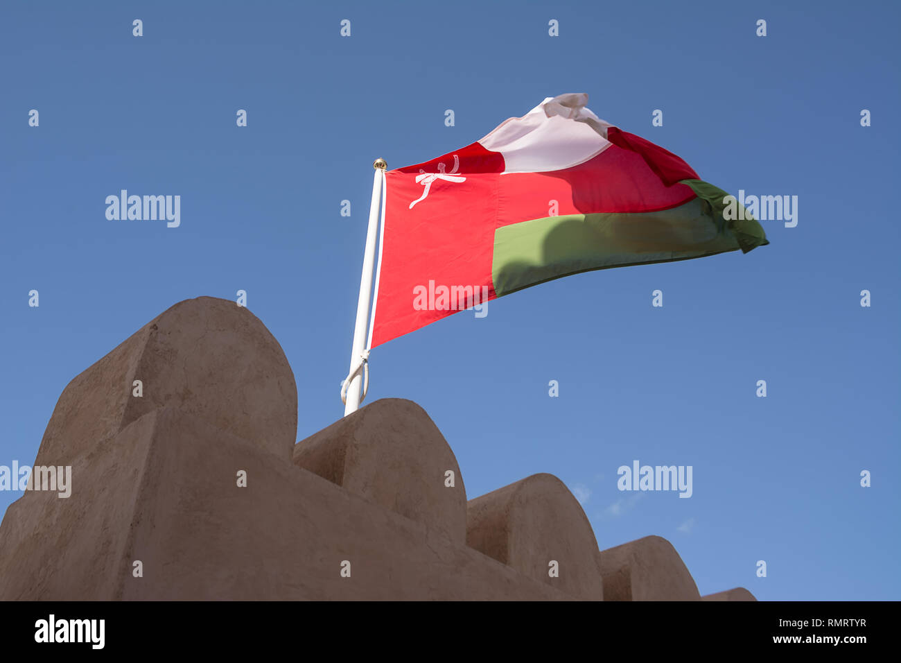 Überbackene Wände der Nahkal Fort und seine Fahne im Wind (Oman) Stockfoto