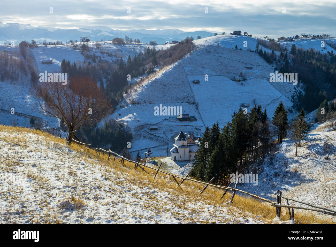 Am frühen Morgen Winter Panorama mit einer Kirche und isolierte Holzhäuser auf verschneiten Hügeln in der ländlichen Gemeinde Magura, Brasov, eine touristische Destination in Stockfoto