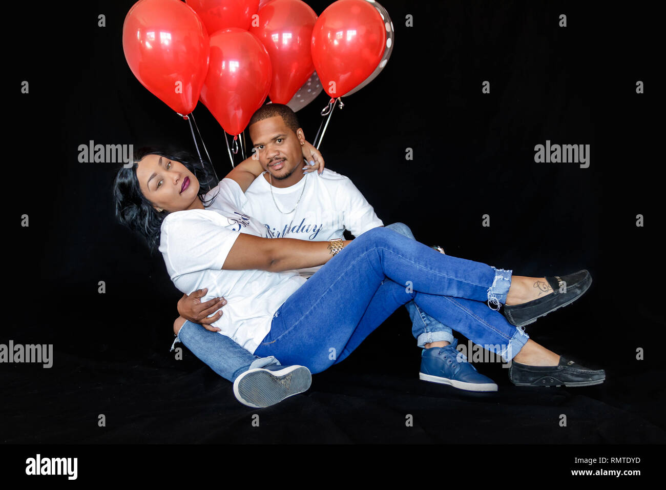 Paar in Blue Jeans mit roten Luftballons ihren Geburtstag feiern gemeinsam spielerisch Stockfoto