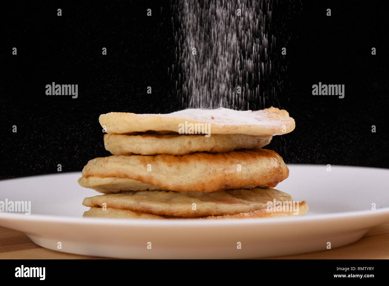Haferflocken bestreuen Pfannkuchen mit Puderzucker. Weiße Platte auf einem hölzernen Hintergrund. Schwarzen Hintergrund. Platz kopieren Stockfoto