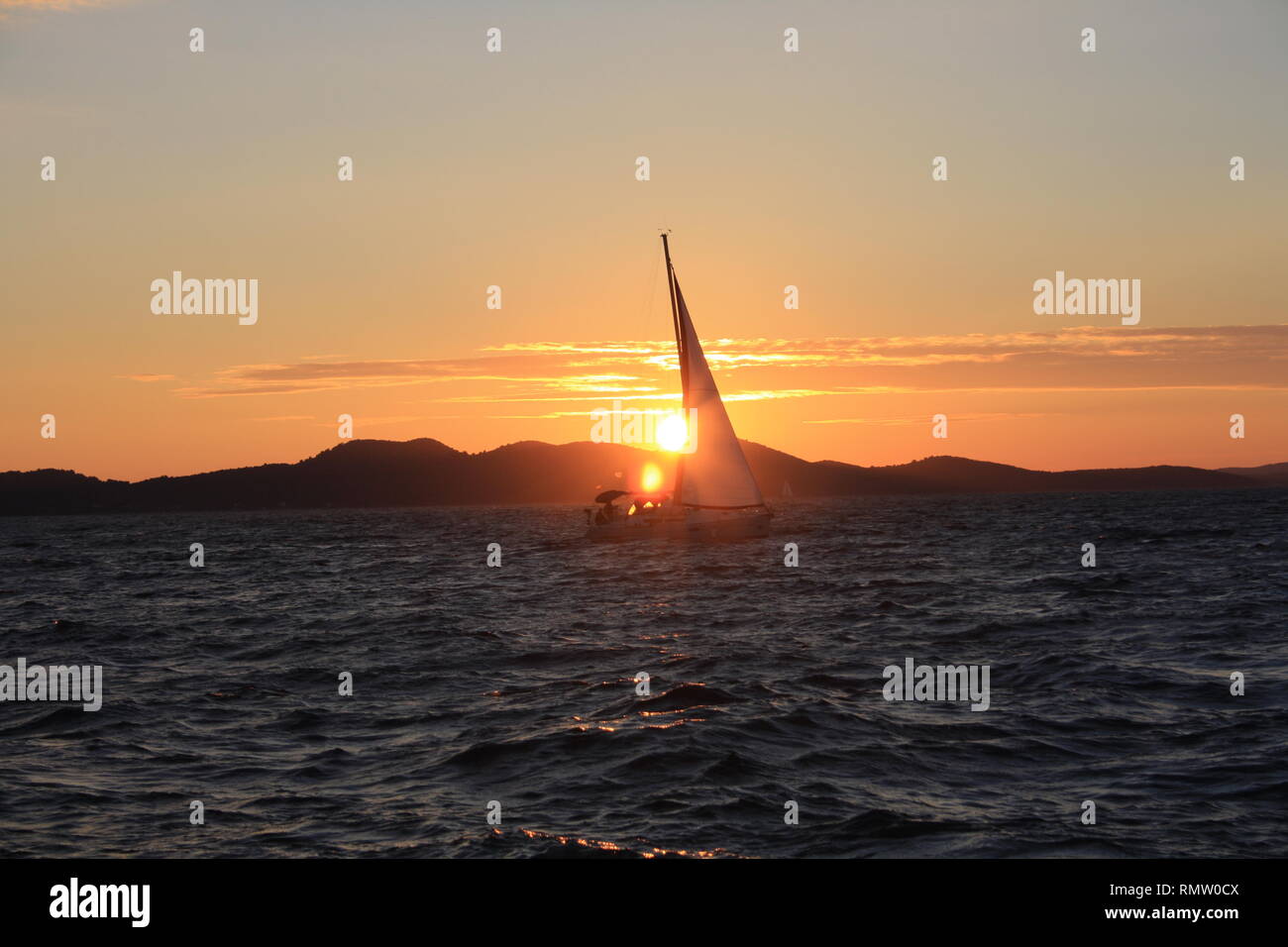 Sonnenuntergang mit Segelboot auf dem Wasser und Bergen im Hintergrund Stockfoto