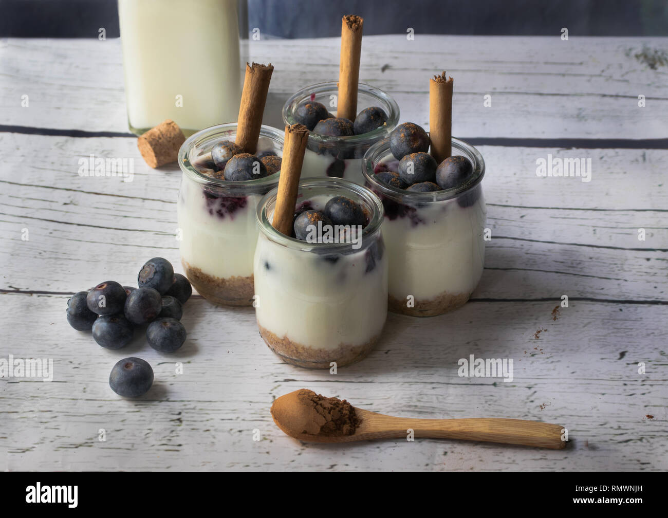 Hausgemachte Joghurt mit Cookies im Hintergrund und Blaubeeren mit Zimt auf ein weißes Holzbrett Stockfoto
