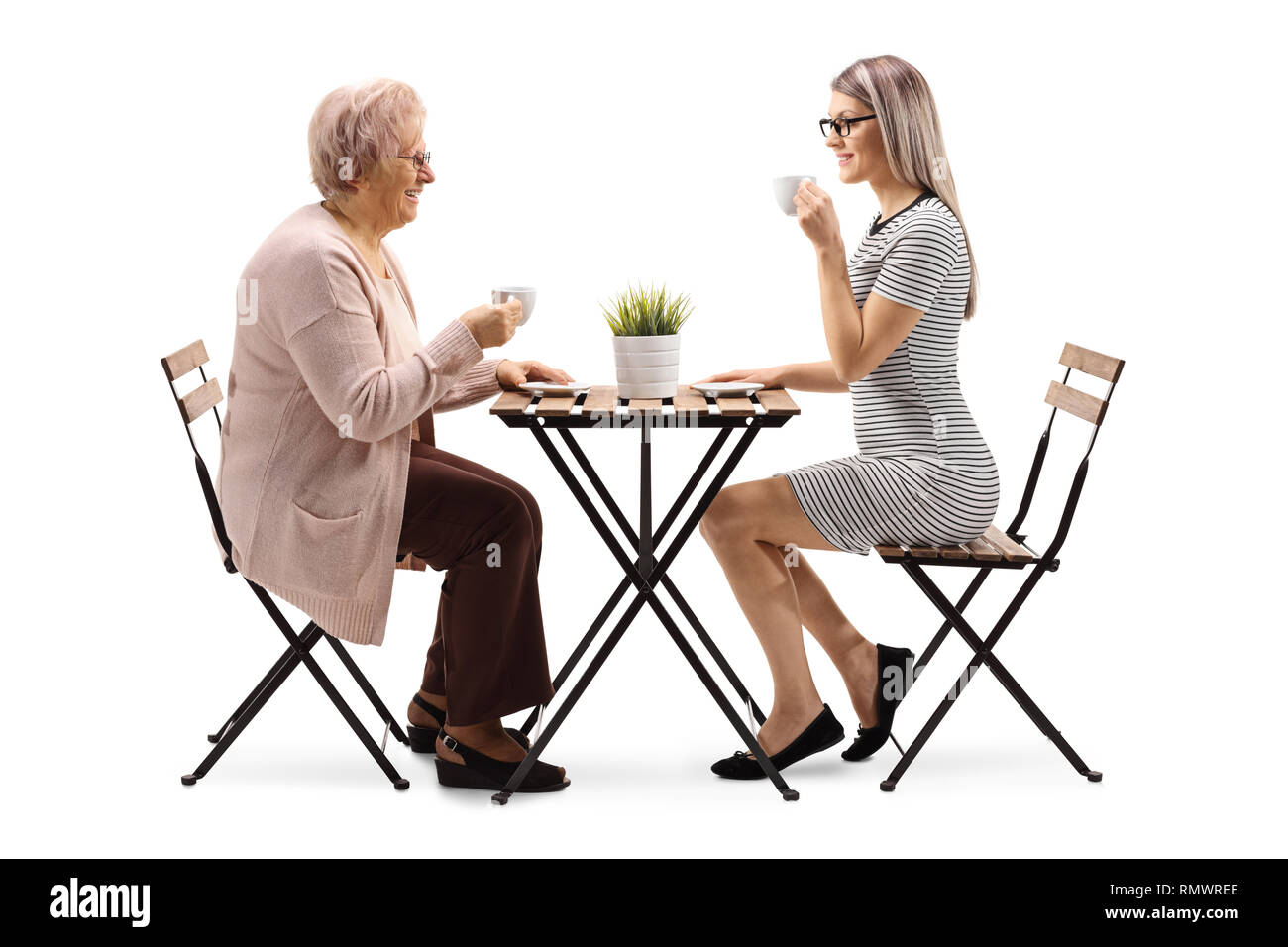 Volle Länge Profil Schuß einer älteren Frau trinkt Kaffee mit einer jungen Frau an einem Tisch auf weißem Hintergrund Stockfoto