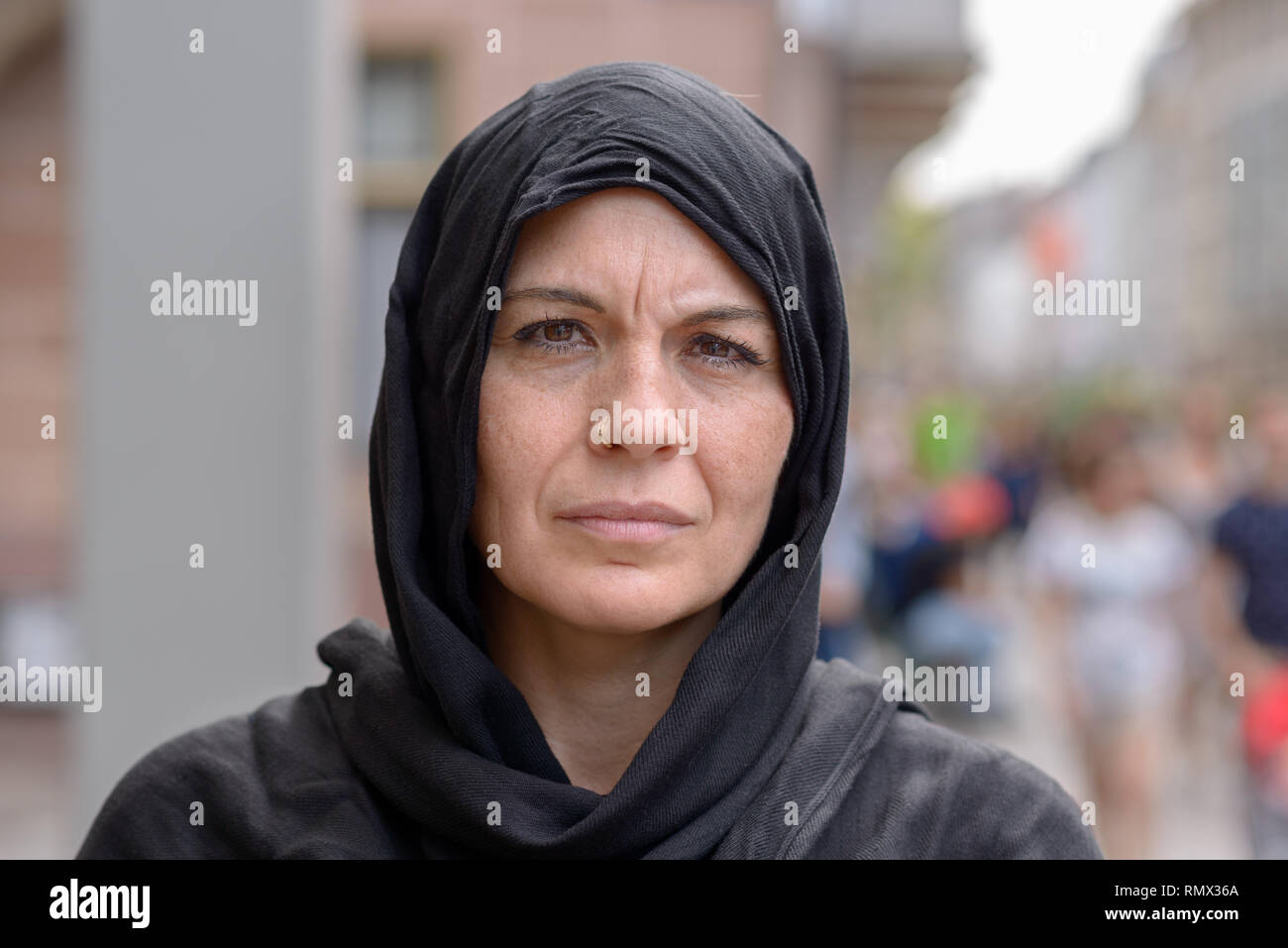 Ernsthafte Frau mittleren Alters, der ein schwarzes Kopftuch oder Hijab in Nahaufnahme Kopf geschossen in einer belebten Straße Stockfoto