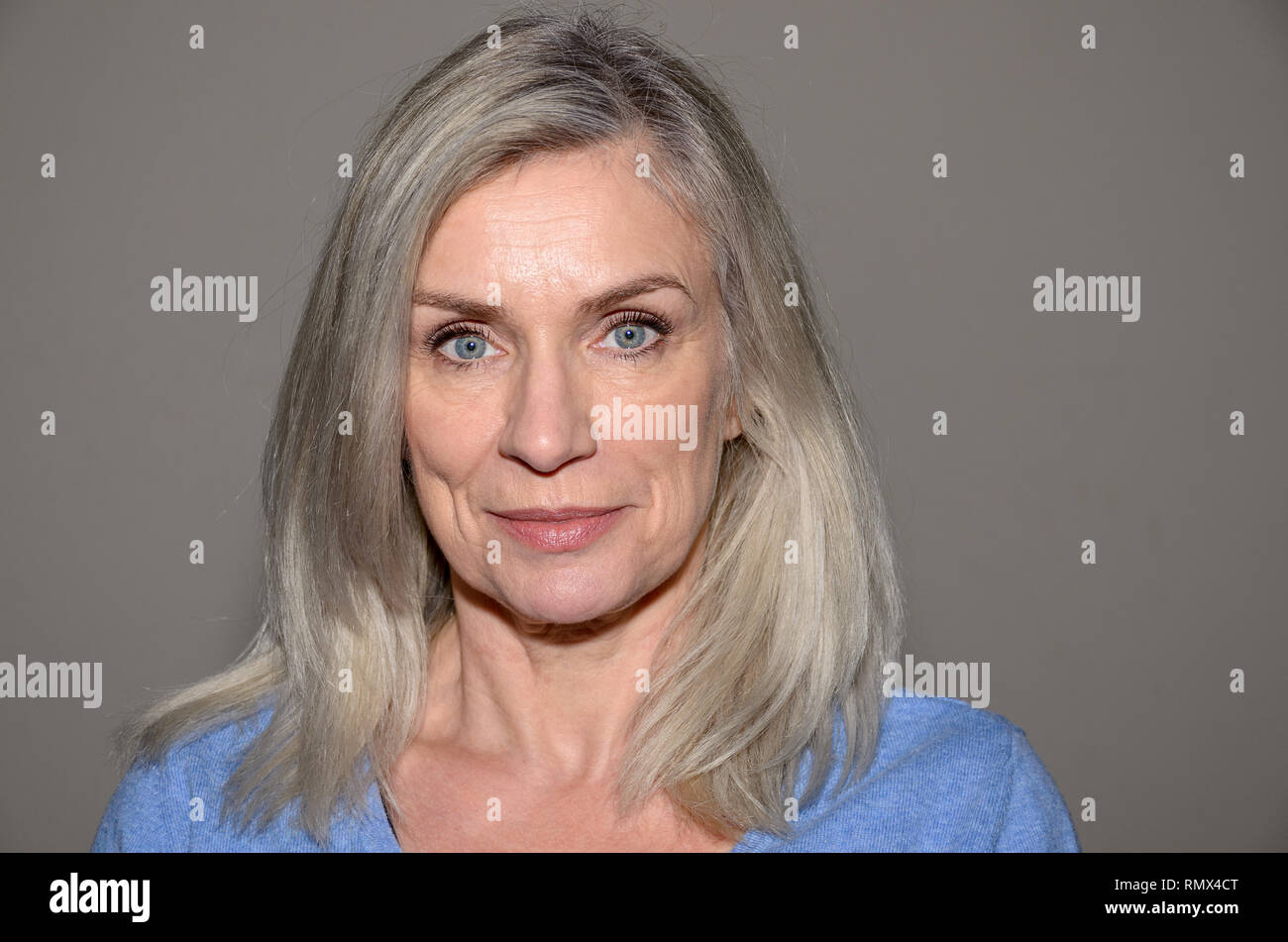 Attraktive blue-eyed blonde Frau mittleren Alters mit einem süßen Lächeln und schulterlanges Haar an Kamera suchen Stockfoto