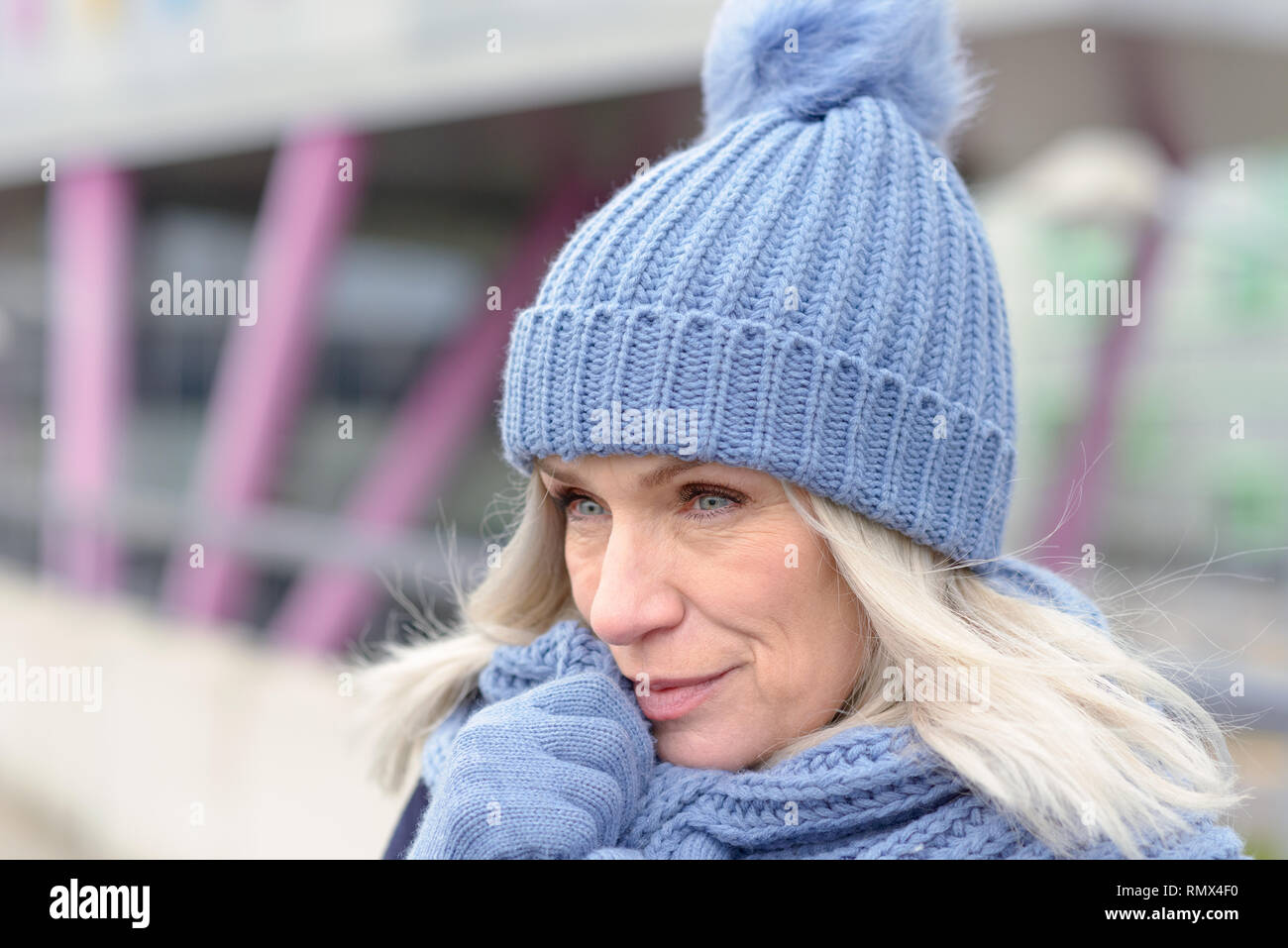 Attraktive blue eyed blonde Frau in passenden Blau warme Winter Fashion trägt eine gestrickte Mütze, Schal und Handschuhe in die Kamera lächeln Stockfoto