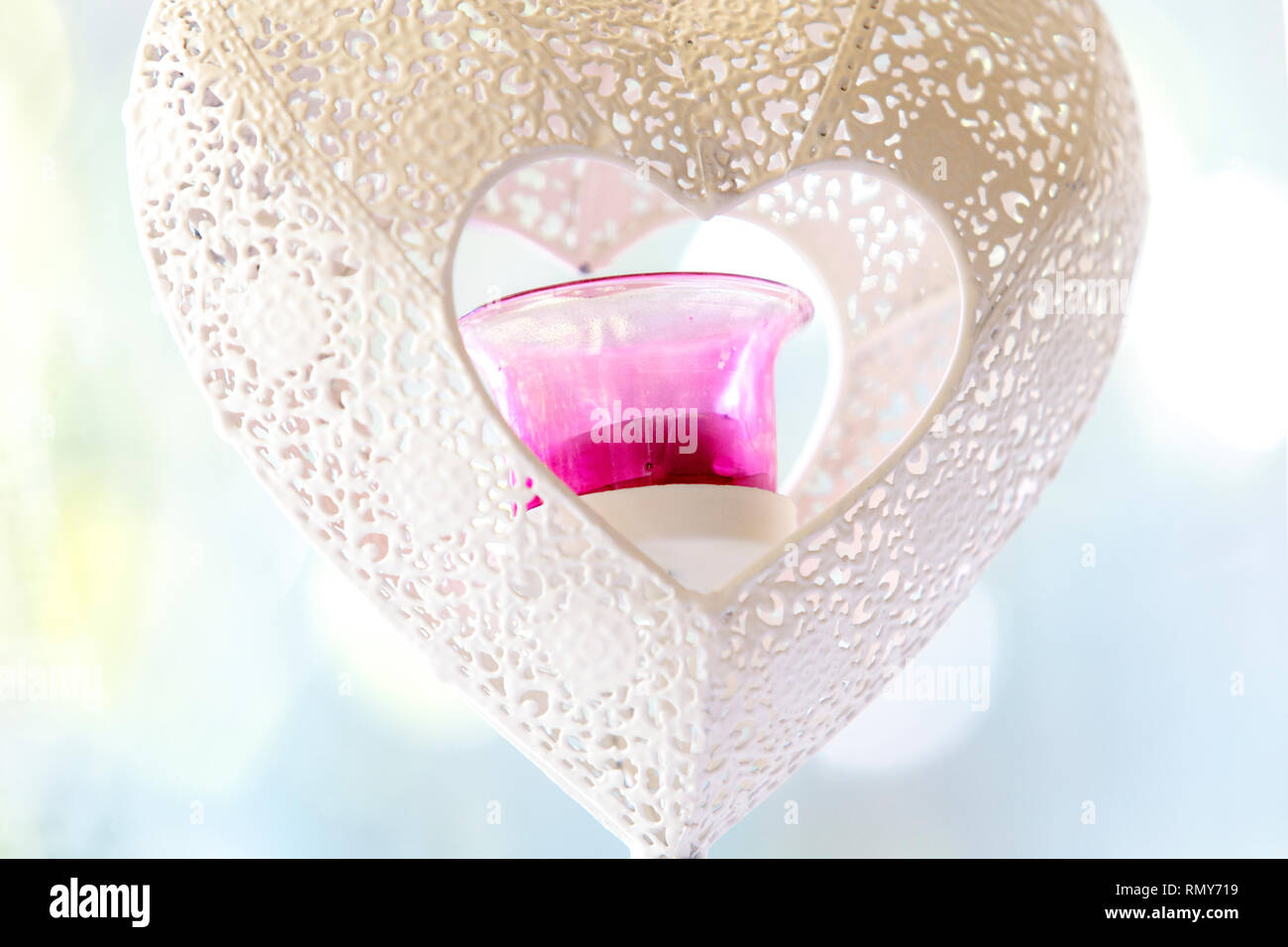 Schließen Sie herauf Bild einer Herzförmigen weiße schmiedeeiserne Kerzenhalter mit rosafarbenen Glas Teelicht isoliert mit schönen Hellblau bokeh. Konzept für die Liebe. Stockfoto