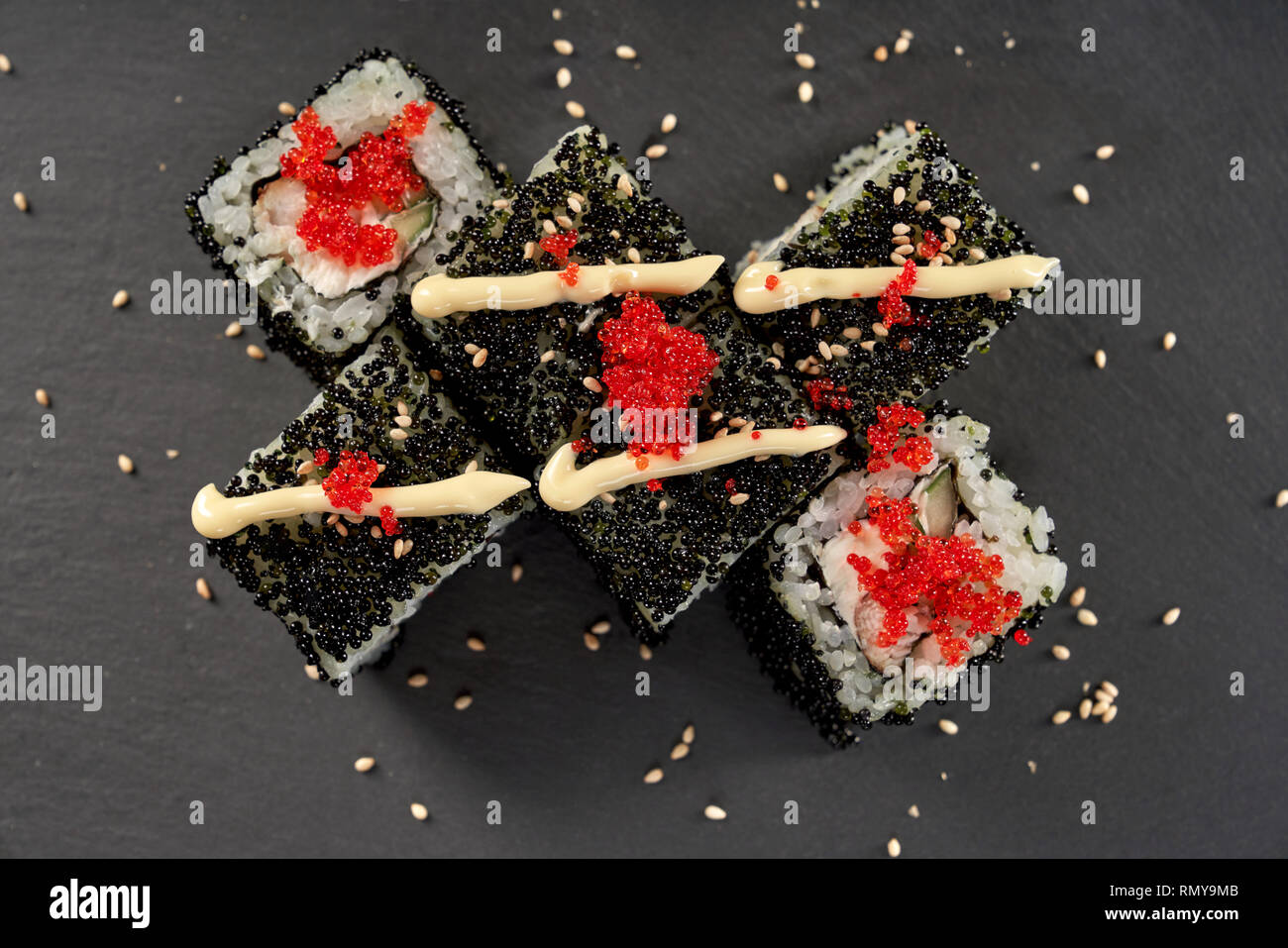 Philadelphia Maki Sushi mit Frischkäse, Gurken und Fisch. Rolle mit Mayo, Rot tobiko Roe und Sesam dekoriert. Ansicht von oben, auf schwarzen Stein Teller serviert. Stockfoto