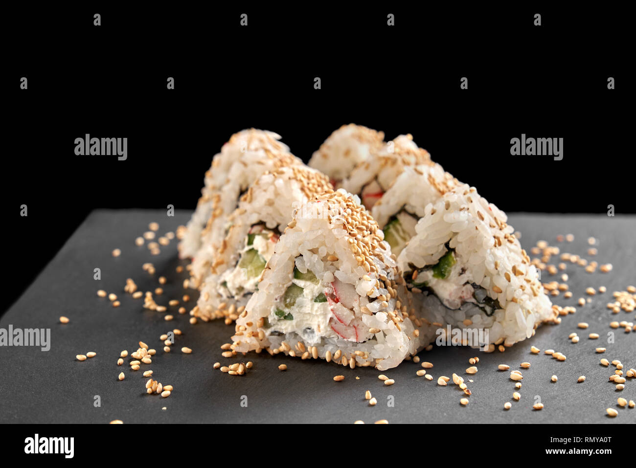 Sushi mit Frischkäse, künstliche Krabbenfleisch und Gurken, mit Sesam abgedeckt. Dreieck uramaki serviert auf schwarzen Stein Schiefer Platte. Stockfoto