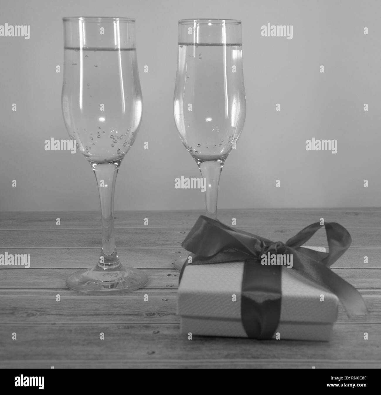 Zwei Gläser mit Champagner und Geschenk Box mit Satinband auf einem Holztisch. Close-up. Stockfoto