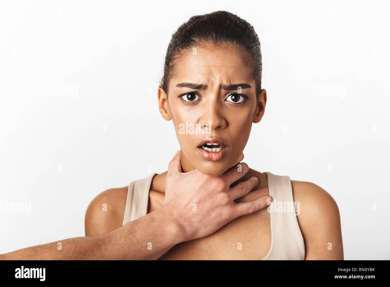 Bild der afrikanischen Übel erschrocken Frau posiert über weiße Wand im Hintergrund, während eine Hand ihren Nacken Holding isoliert. Stockfoto