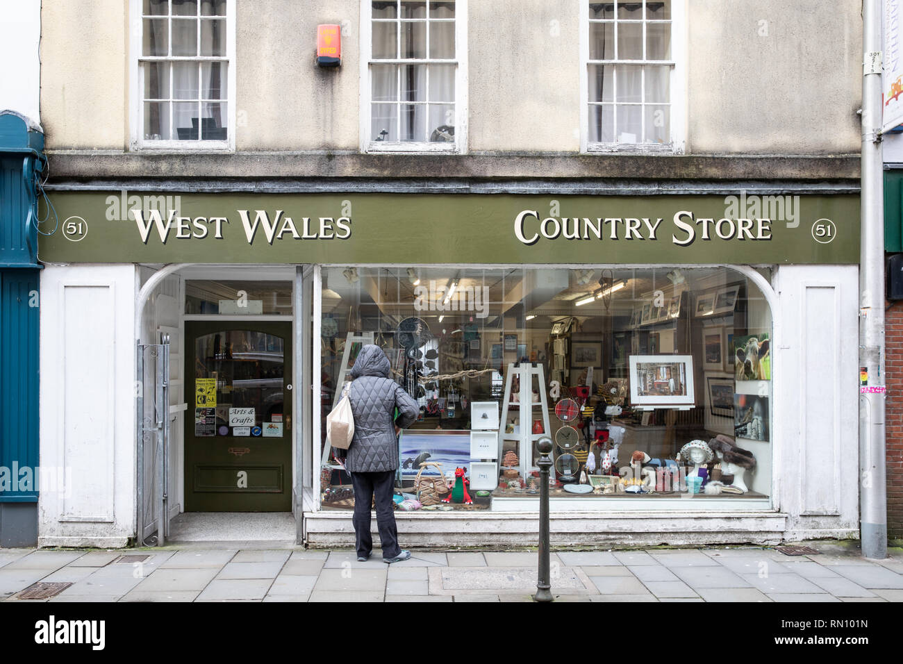 Eine Dame schaut durch die Fenster an der West Wales Country Store Shop in Kings Street Carmarthen. Sie verkaufen die Landschaft im Freien. Stockfoto