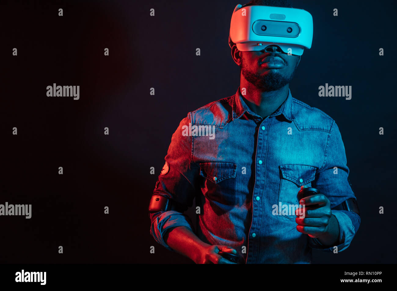 Nicht erkennbare jungen afrikanischen Mann spielt Video Spiel tragen Virtuelle Realität Gerät gegen Rot und Blau Dual Color Licht auf dunklem Hintergrund. Gaming eq Stockfoto