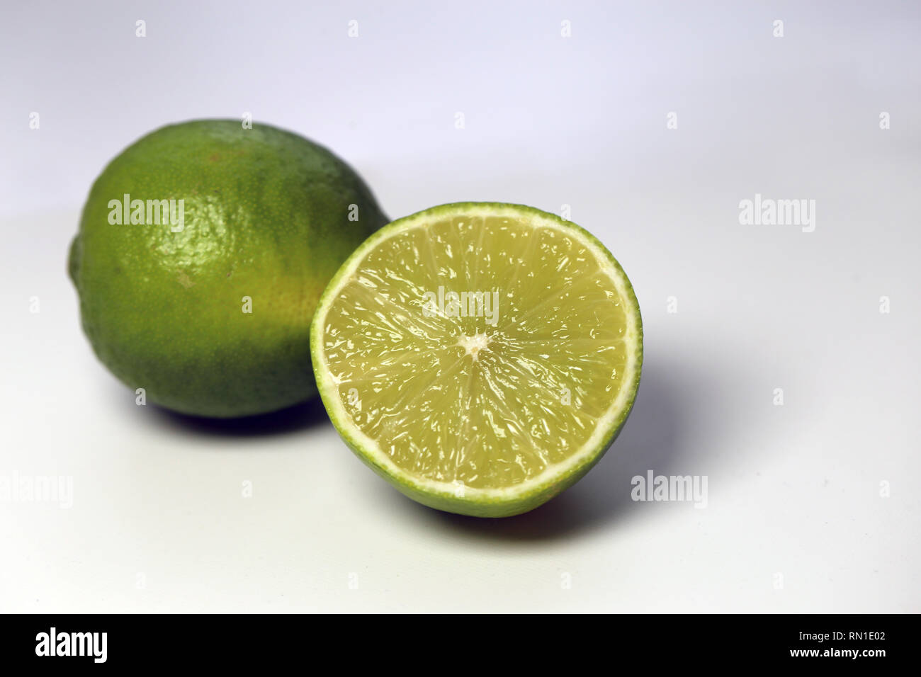 Eine Nahaufnahme von zwei saftig, reife Limetten. Eine Kalk wird halbiert. Auf einem weißen Tisch fotografiert. Foto mit einem Makro Objektiv aufgenommen. Stockfoto