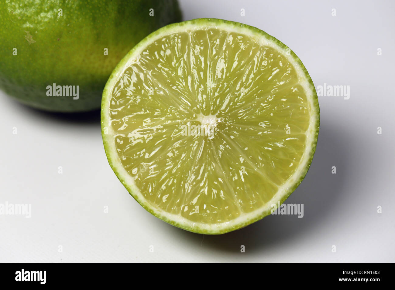 Eine Nahaufnahme von zwei saftig, reife Limetten. Eine Kalk wird halbiert. Auf einem weißen Tisch fotografiert. Foto mit einem Makro Objektiv aufgenommen. Stockfoto