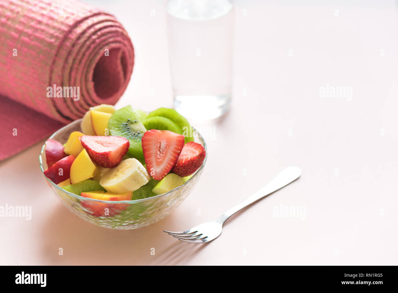 Feminine Sport und gesunder Lebensstil Konzept. Rosa Yoga Matte und Obst und Beeren Salat in der Schüssel für Snack oder Frühstück auf Rosa pastell Hintergrund, kopieren Stockfoto
