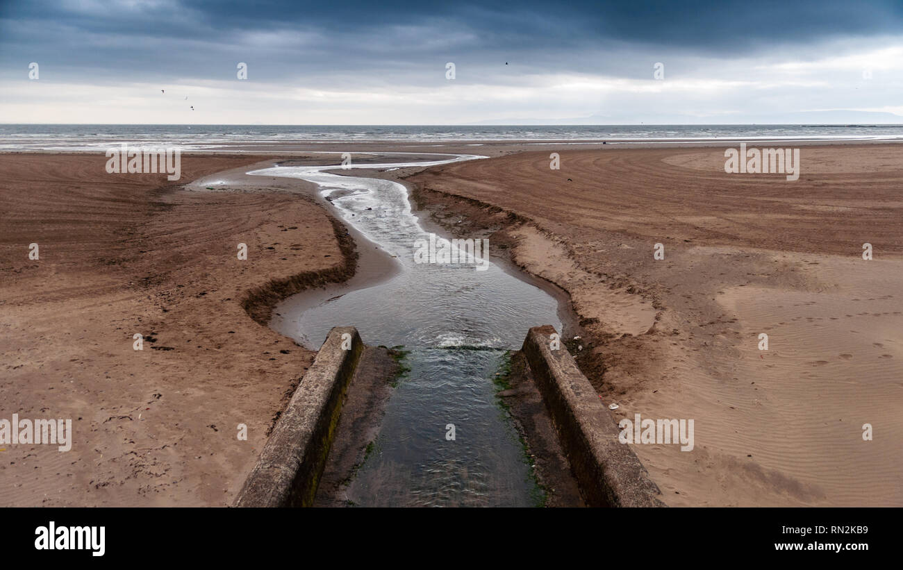 Ein kleiner Fluss schneidet einen Kanal über der Sandstrand in Saltcoats und Ardrossan auf die Forth Clyde Strand in Ayrshire. Stockfoto