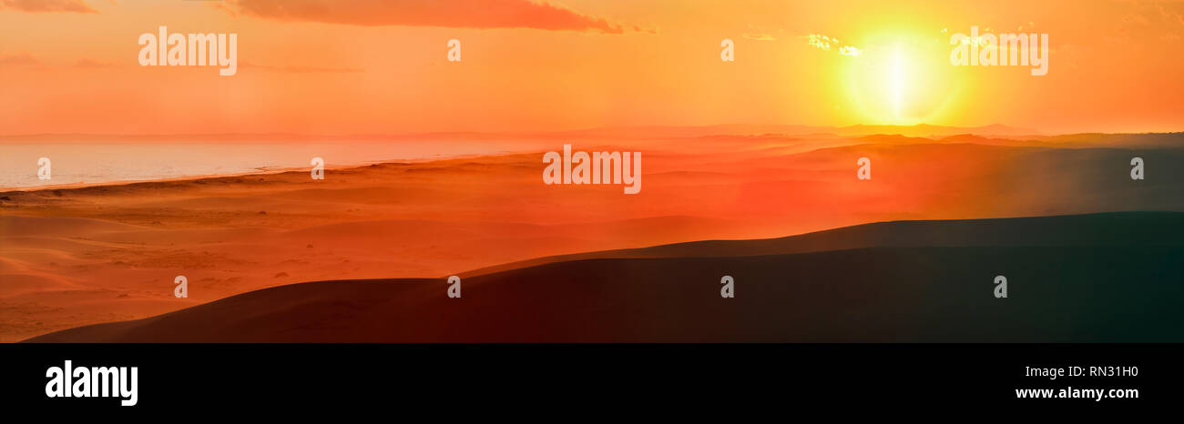 Orange helle rötliche Sonnenuntergang über dem Horizont von Sanddünen von Stockton Strand von Pacific Coast in Australien gesehen. Breites Panorama über Sand dune reicht. Stockfoto