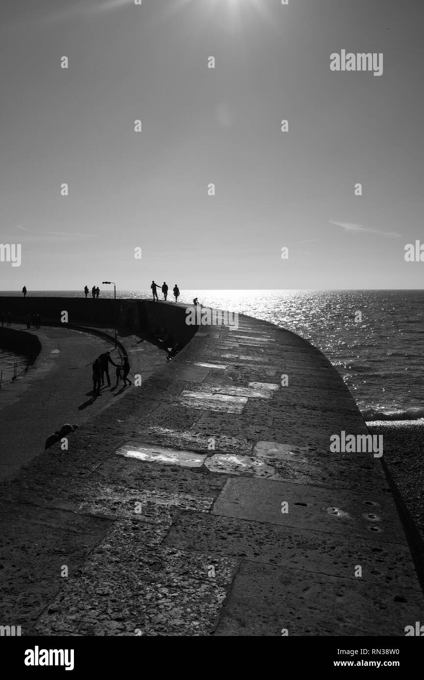 Lyme Regis Cob sweeps heraus zum Meer, schwarz-weiß-Bild in einem Porträt Aspekt mit den Menschen auf der Cob in der Ferne Stockfoto